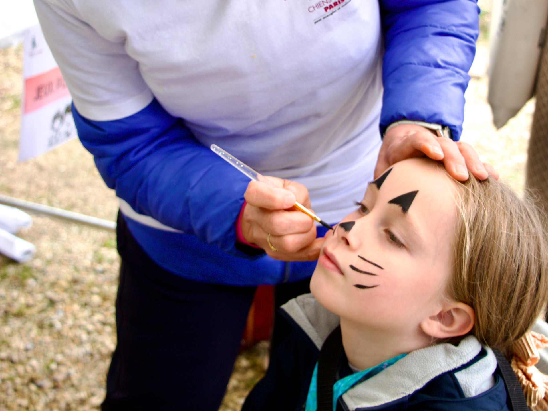 une bénévole réalise un maquillage de chat sur une enfant