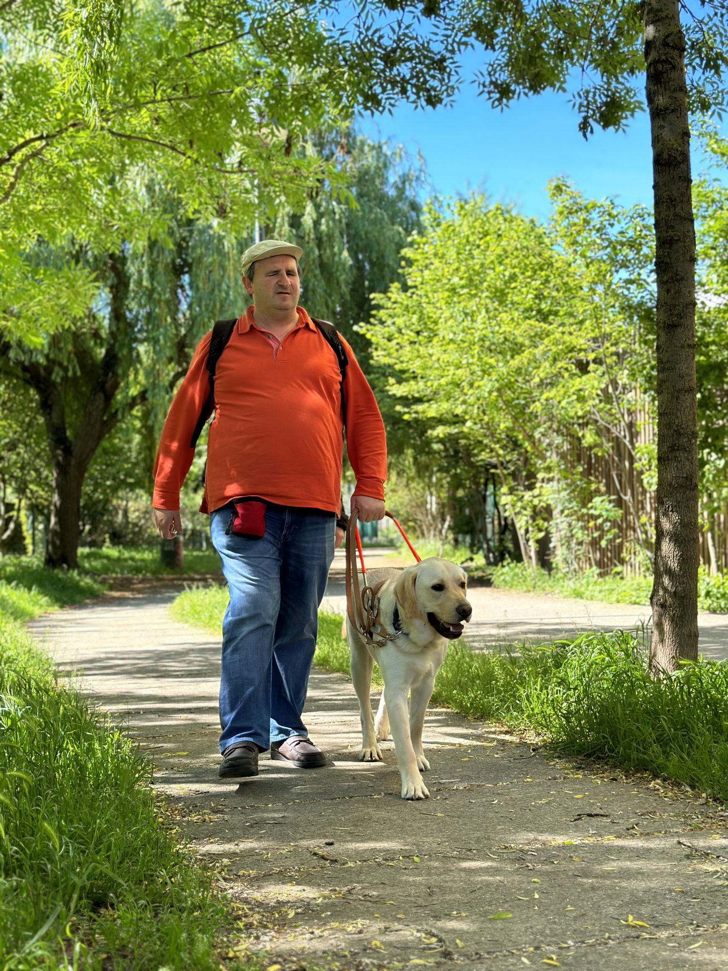 Jean-Pierre, personne malvoyante et Scratt son chien guide se promenant dans un parc ombragé